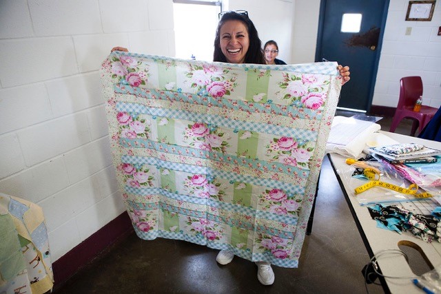 smiling inmate holding up a floral quilt top